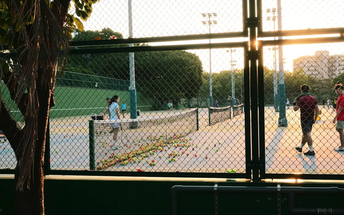 Public tennis courts at golden hour with players and spectators on a warm summer evening