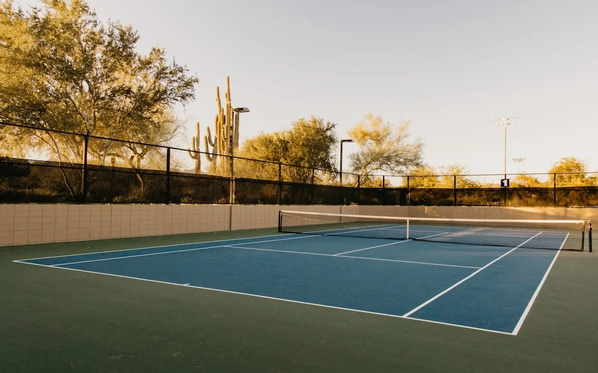 An empty blue hard court at golden hour with the net up and the floodlights waiting