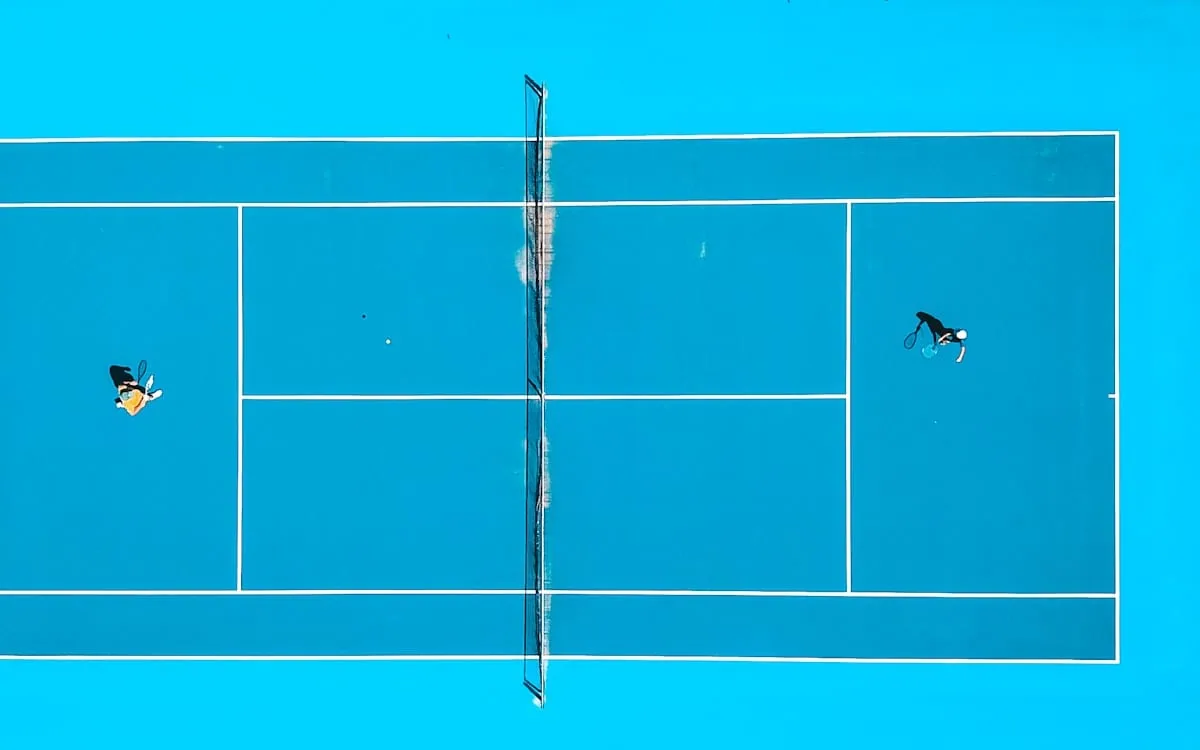 A blue hard court seen from directly above with two players at opposite baselines, the view that suits a US Open underdog story