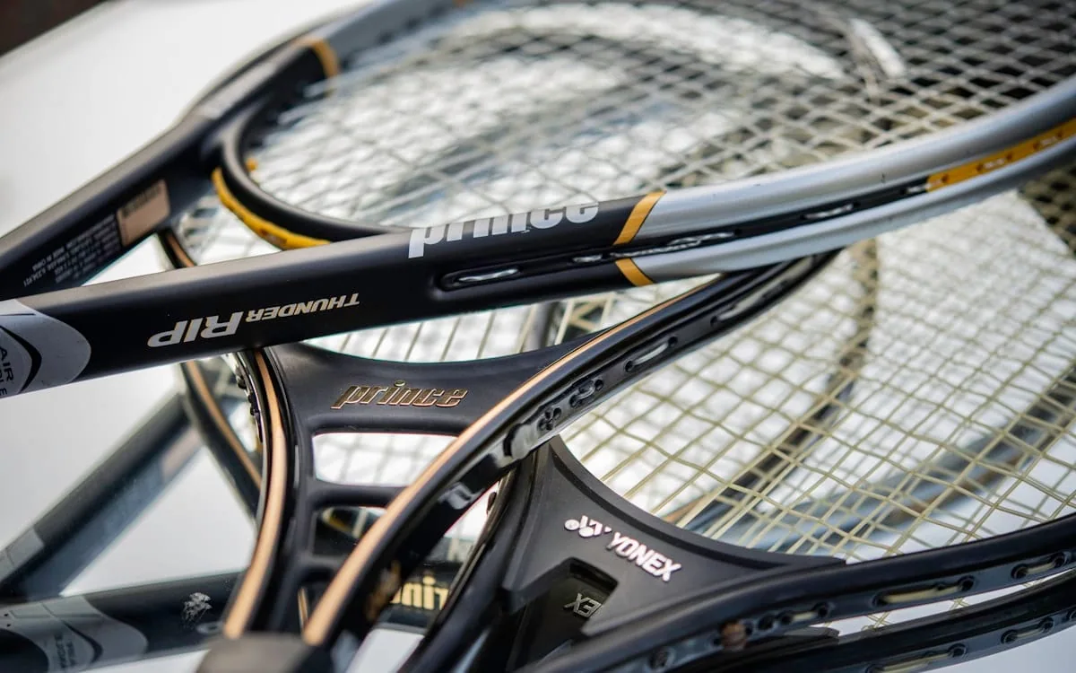 A pile of well used tennis rackets stacked one on top of another, frames and strings catching the light