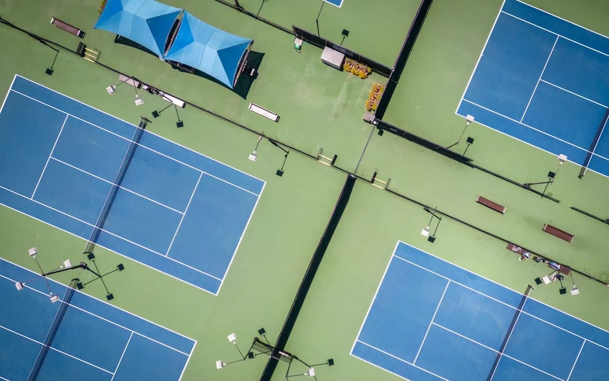 An aerial view of empty blue hard courts at a tennis complex, the kind of outside courts used at a small ATP tournament
